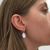 Silver drop earrings with shell fossil imprint which hang from a small bar that conceals the post and butterfly behind. Earrings are shown on a model - profile image.