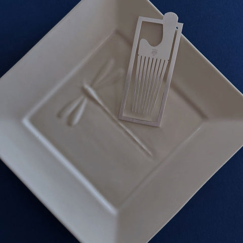 Silver bookmark shown resting on a white dish.