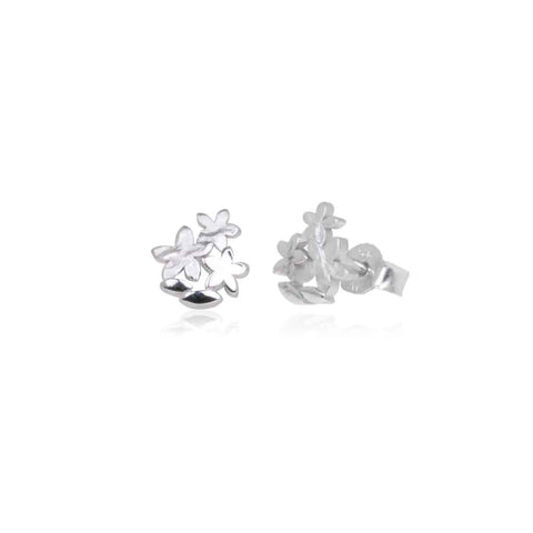 Sterling silver stud earrings in the shape of petite flowers. Shown sitting on a table with a shadow.