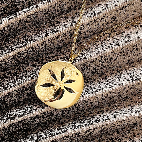 Gold pendant necklace shown flat on textured fabric.